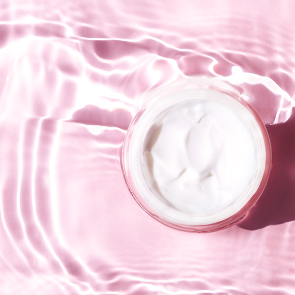 Crème visage postbiotique blanche dans un pot sur fond rose, soin hydratant et apaisant.